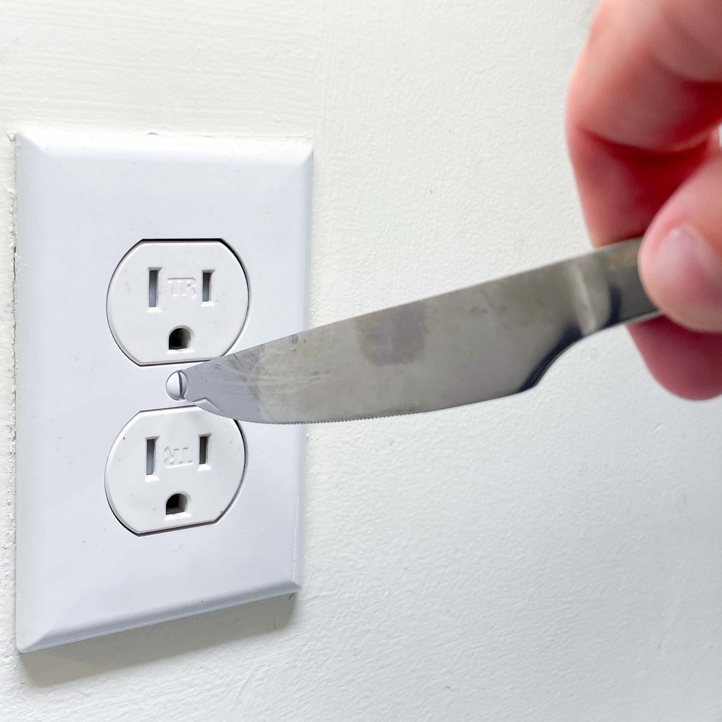 Hand Holding a Knife Tightening an Outlet Screw